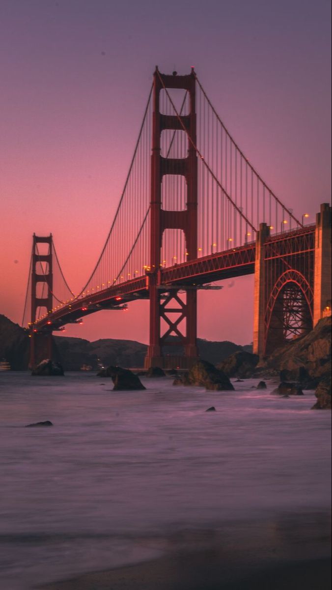 the golden gate bridge in san francisco, california at sunset with lights reflecting off the water