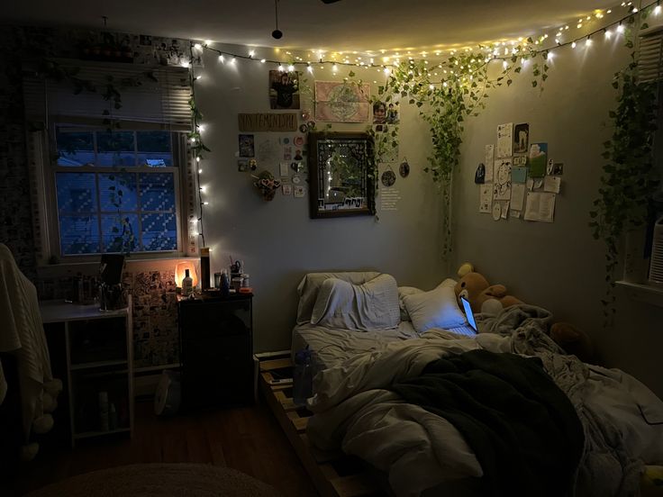 an unmade bed in a bedroom with lights strung from the ceiling and plants on the wall