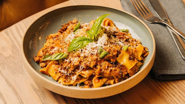 a plate of pasta with meat and parmesan cheese on the side next to a fork