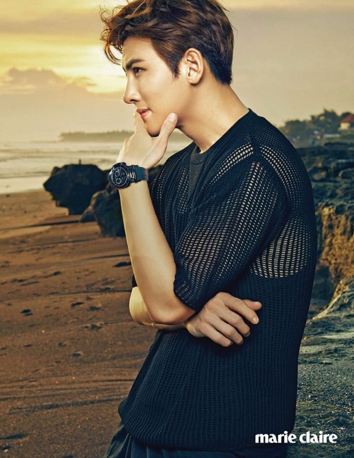 a young man standing on top of a beach next to the ocean with his hand under his chin