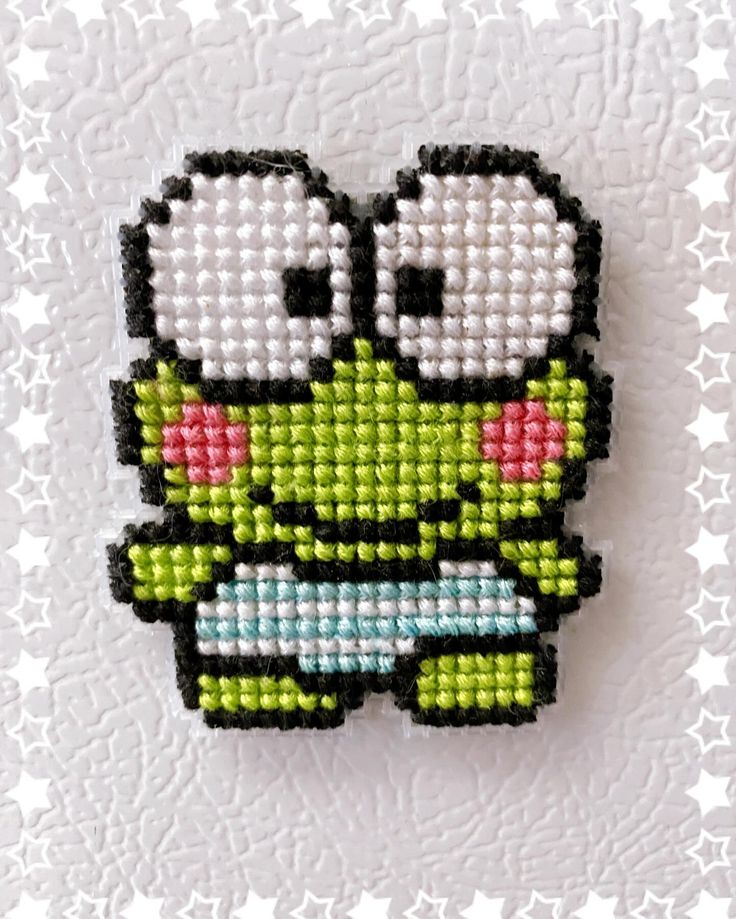 a cross stitched brooch with an image of a green monster on it's face