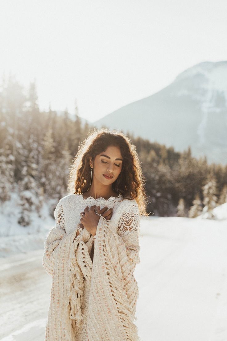 a woman standing in the snow wearing a white sweater