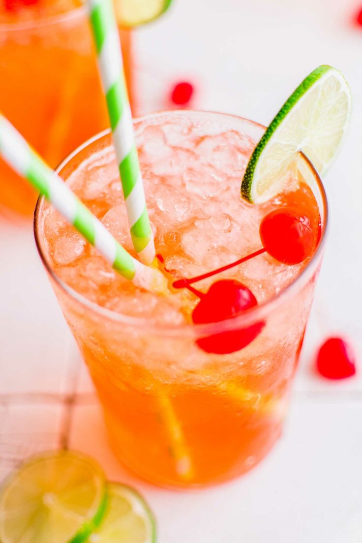 two glasses filled with drinks and garnished with limes, cherries, and lemon wedges