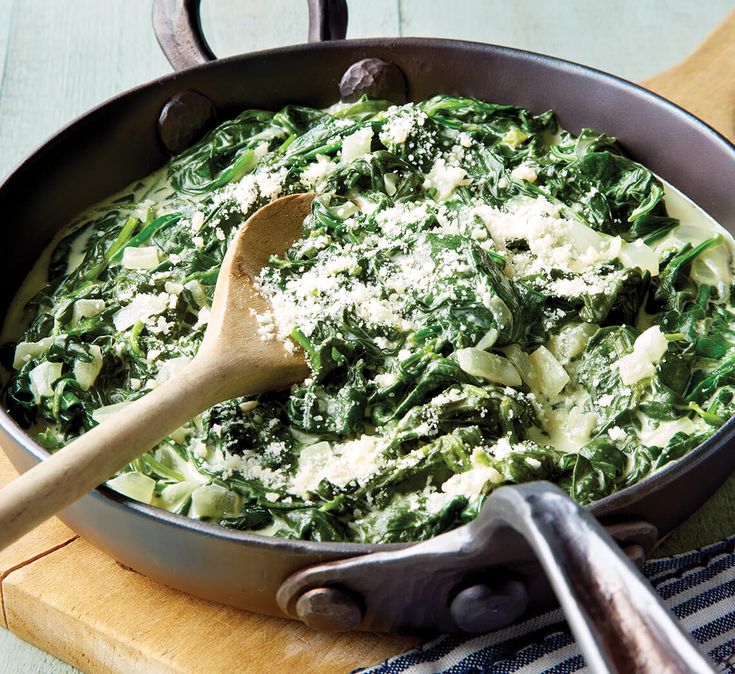 a pan filled with spinach and cheese on top of a cutting board next to a wooden spoon