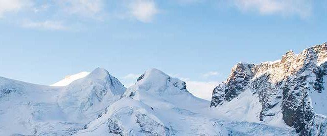 two people on skis are standing in the snow with mountains in the back ground