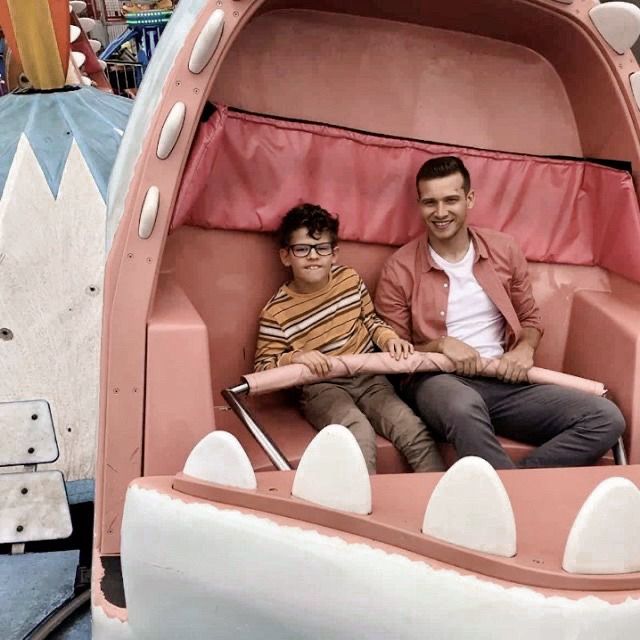 two men sitting in a pink and white boat shaped like a dragon at an amusement park