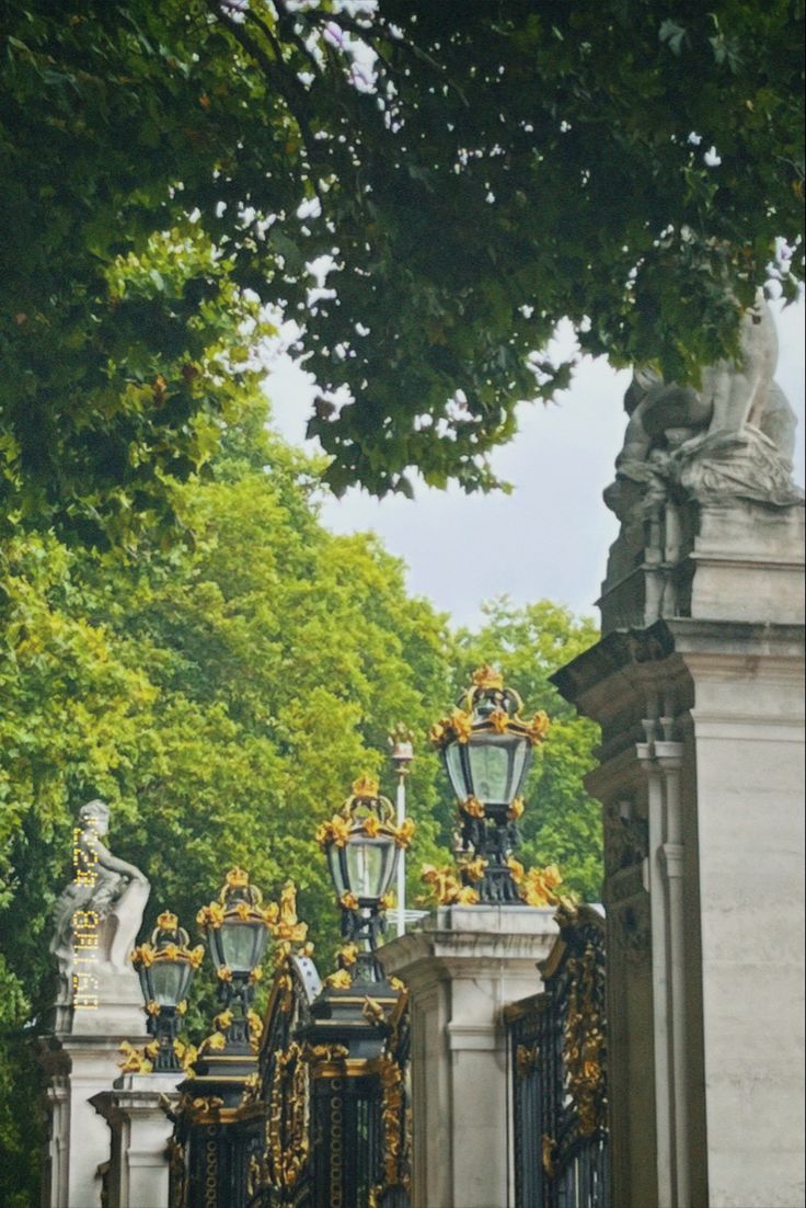 an iron gate with statues on it and trees in the background