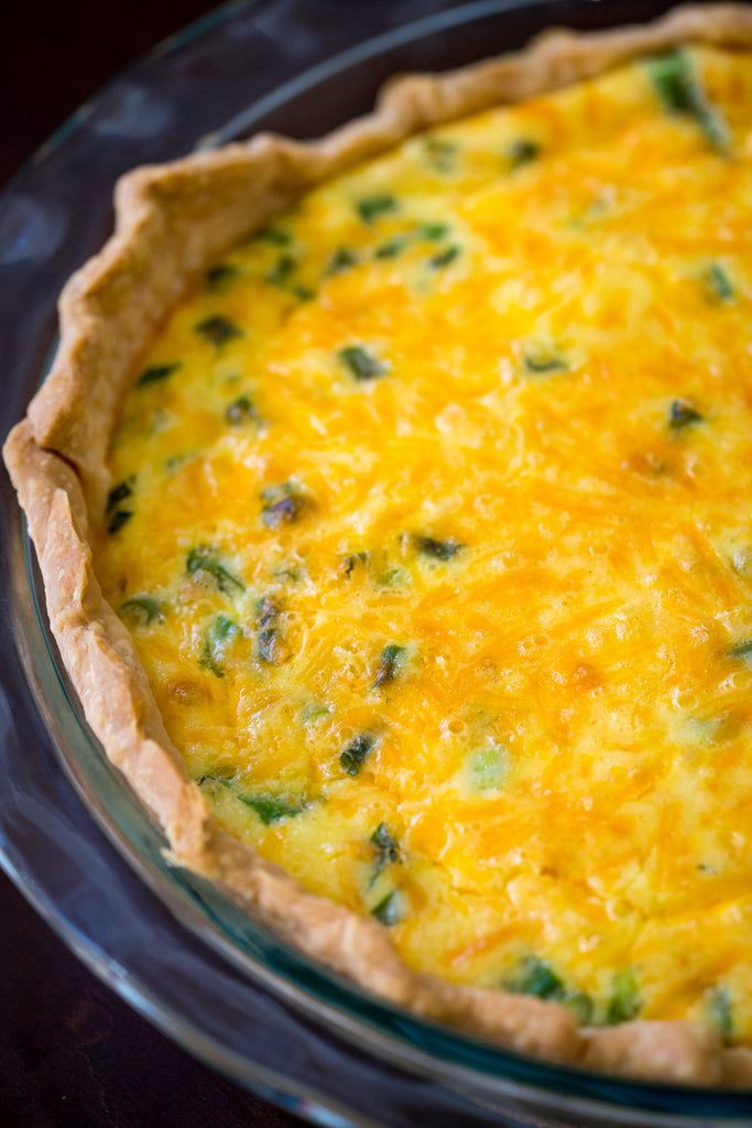 a quiche with cheese and broccoli in a glass pie dish on a table