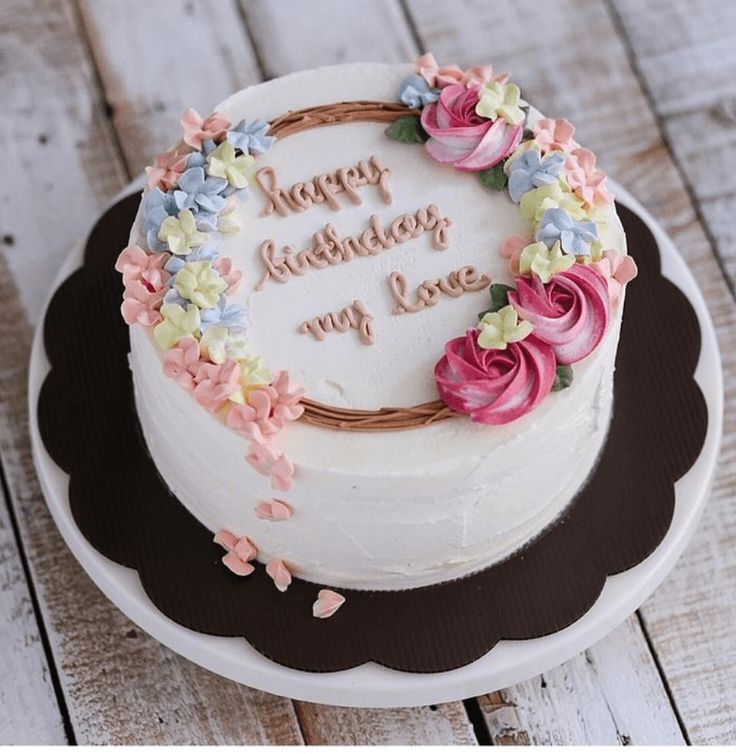 a birthday cake with flowers on it sitting on a wooden table next to a sign that says your good name