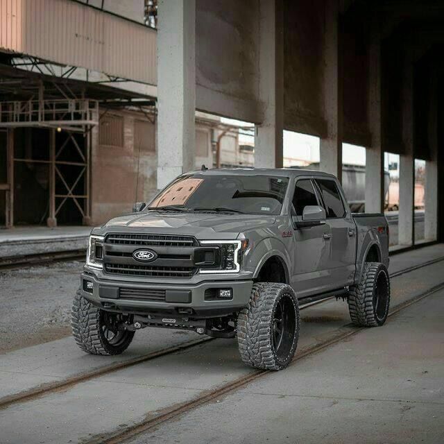 a gray truck is parked in front of a building with large tires on it's wheels