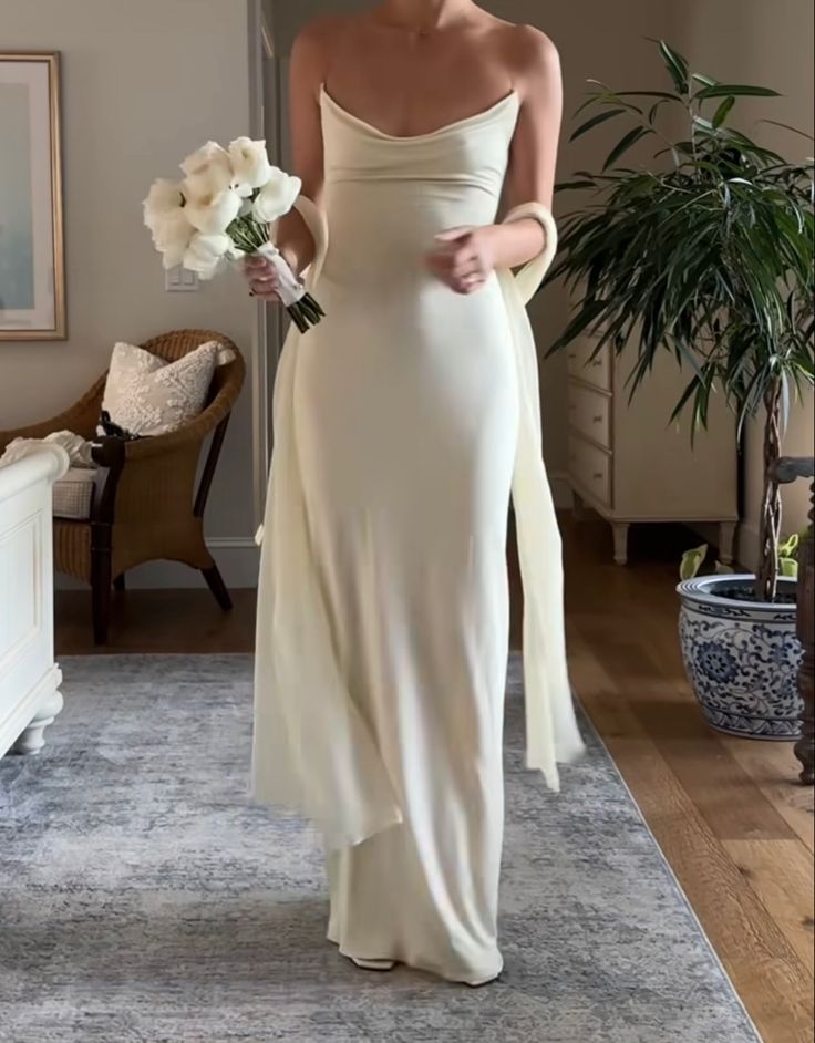 a woman in a white dress is holding flowers and looking at the camera while standing on a rug