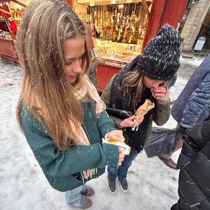 two girls eating food in the snow while another girl looks at her phone and smiles