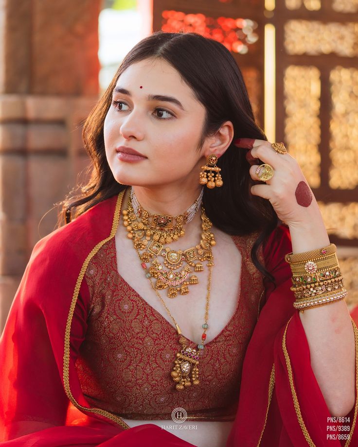 a woman in a red outfit with gold jewelry on her neck and hands behind her head