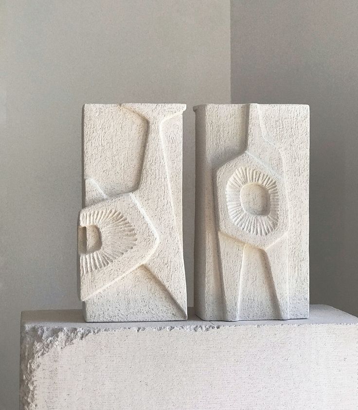 two white sculptures sitting on top of a cement block in front of a gray wall