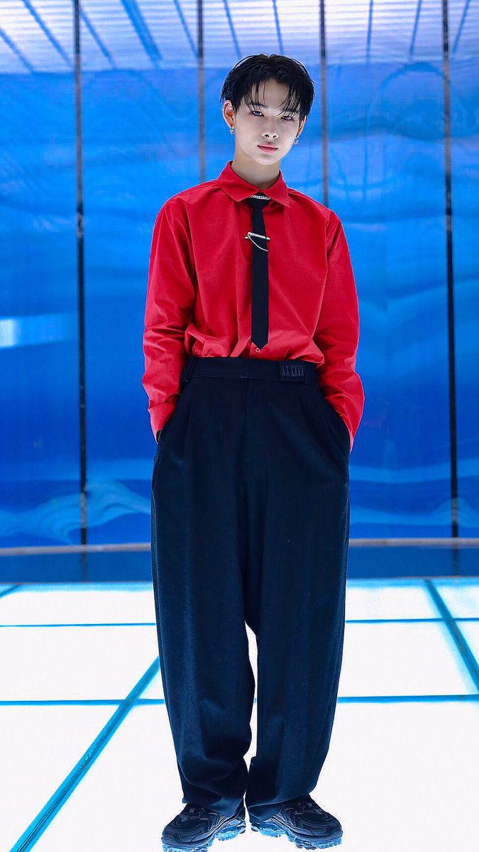 a young man in a red shirt and black tie standing with his hands on his hips