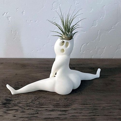 a small white ceramic planter with an air plant on it's head and legs