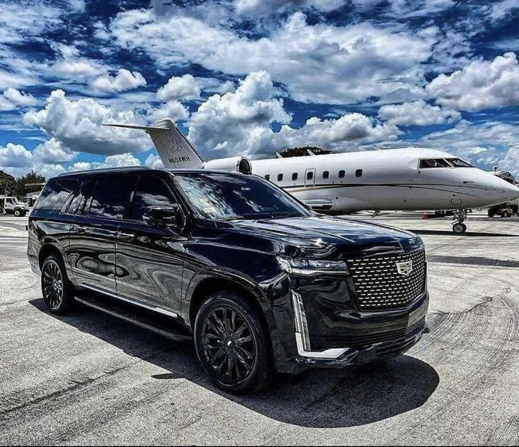 a black suv parked in front of an airplane on the tarmac with another plane behind it