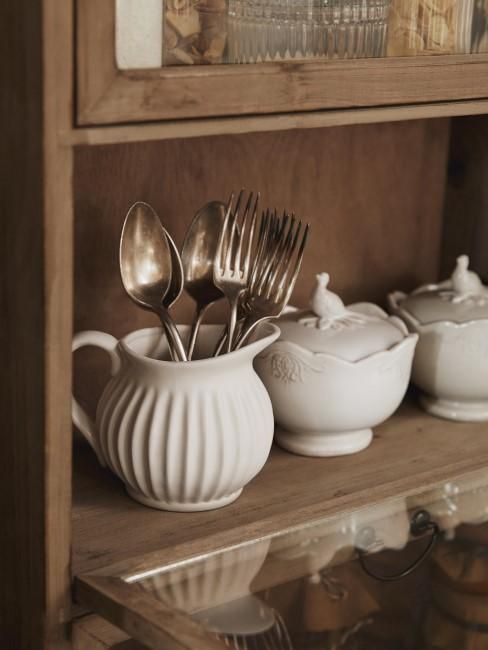 spoons and utensils are sitting in white dishes on a shelf next to other items