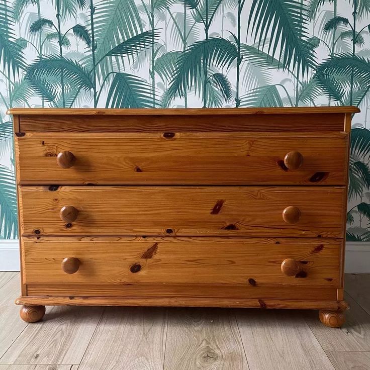 a wooden dresser sitting in front of a wall with palm leaves painted on the walls