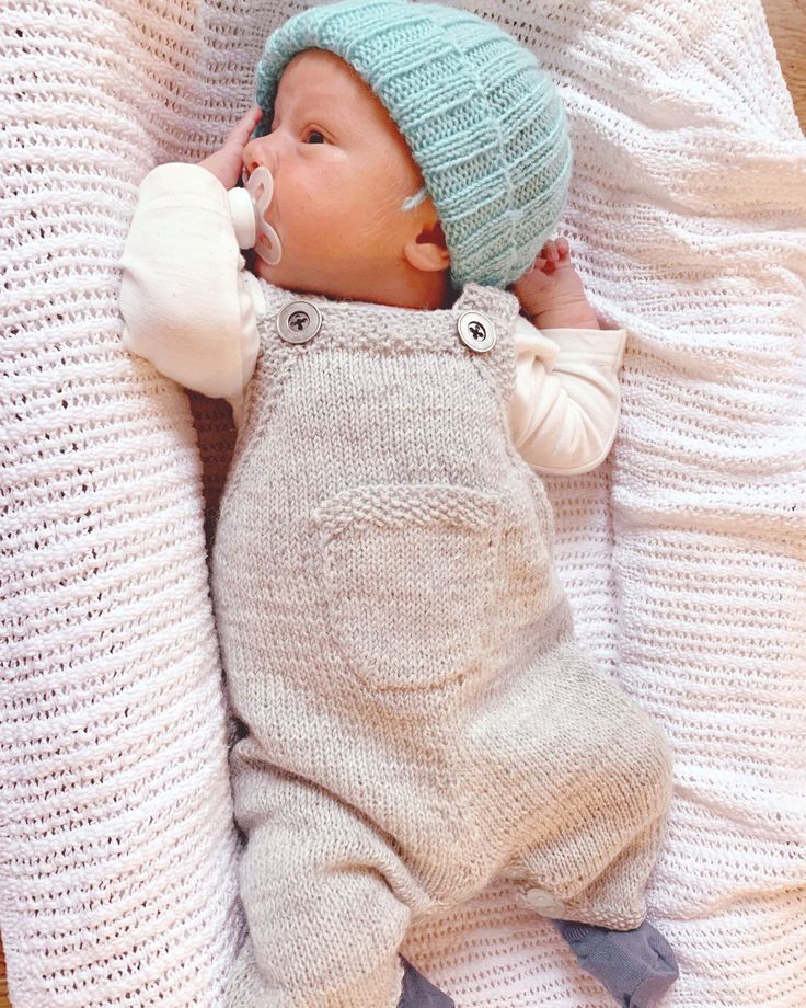 a baby laying on top of a white blanket next to a stuffed animal and wearing a knitted hat