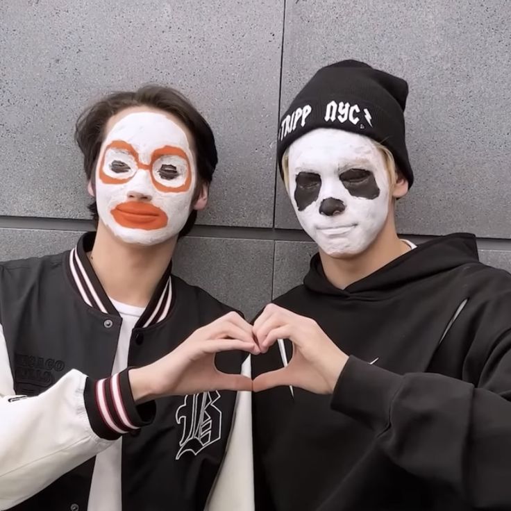 two people with painted faces standing next to each other in front of a gray wall