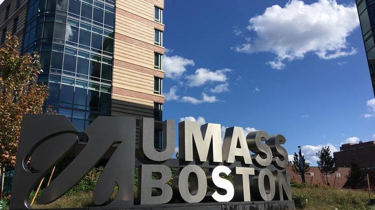 a large metal sign that says umass boston in front of a tall building on a sunny day