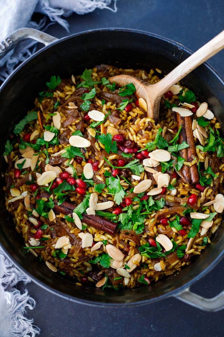 a pot filled with rice and vegetables on top of a blue table cloth next to a wooden spoon