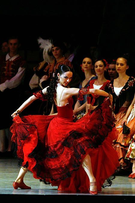 two women in red dresses are dancing on stage with other dancers behind them and people watching