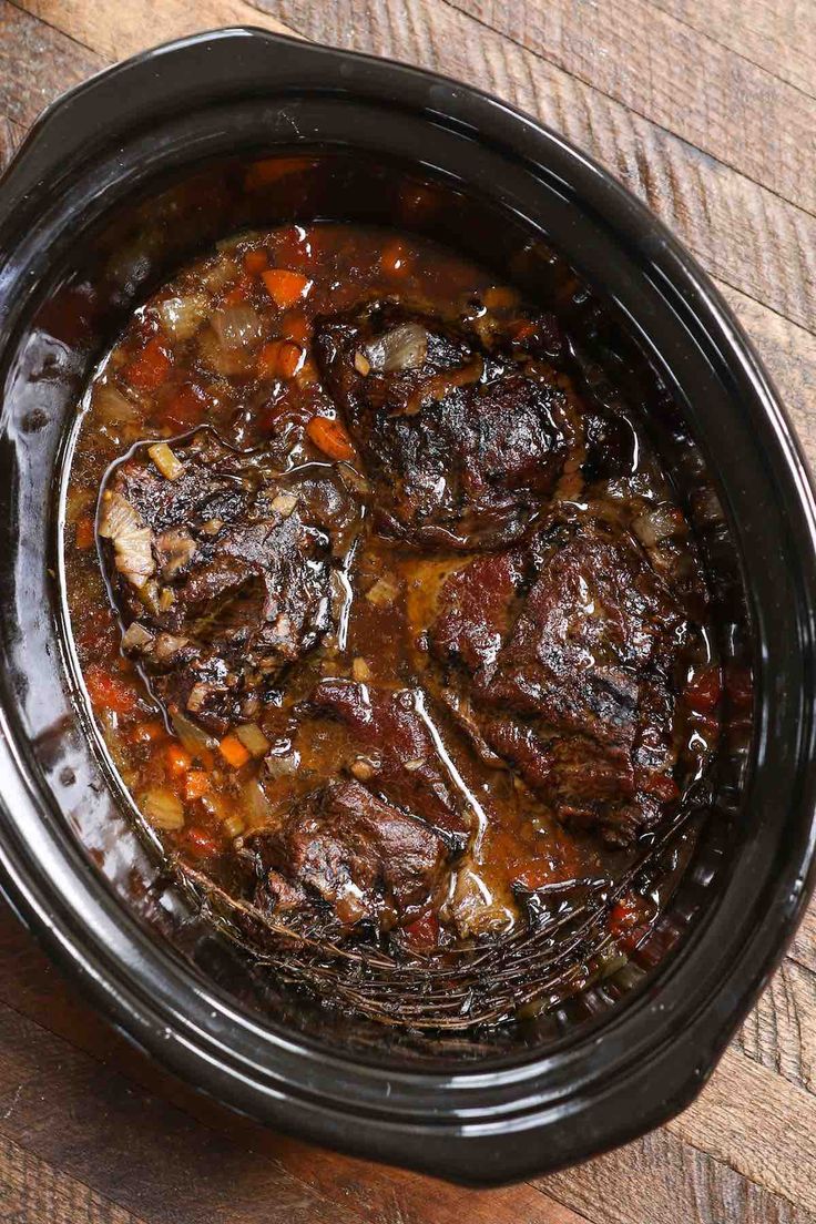 a crock pot filled with beef stew on top of a wooden table