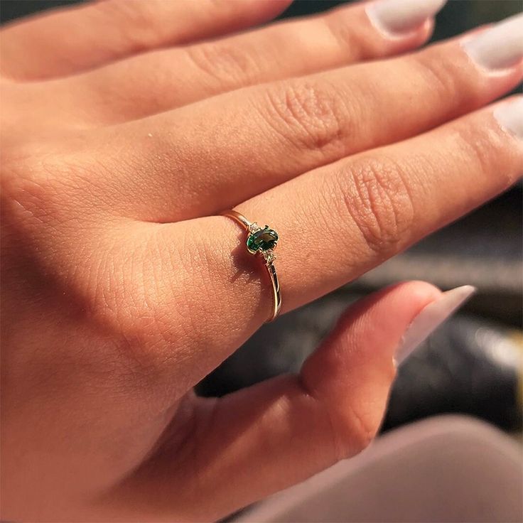 a woman's hand with a gold ring and green gems on it, while she is wearing white nail polish