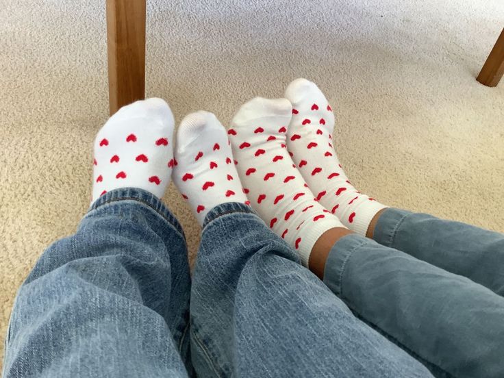 two people wearing white socks with red hearts on them sitting in front of a table