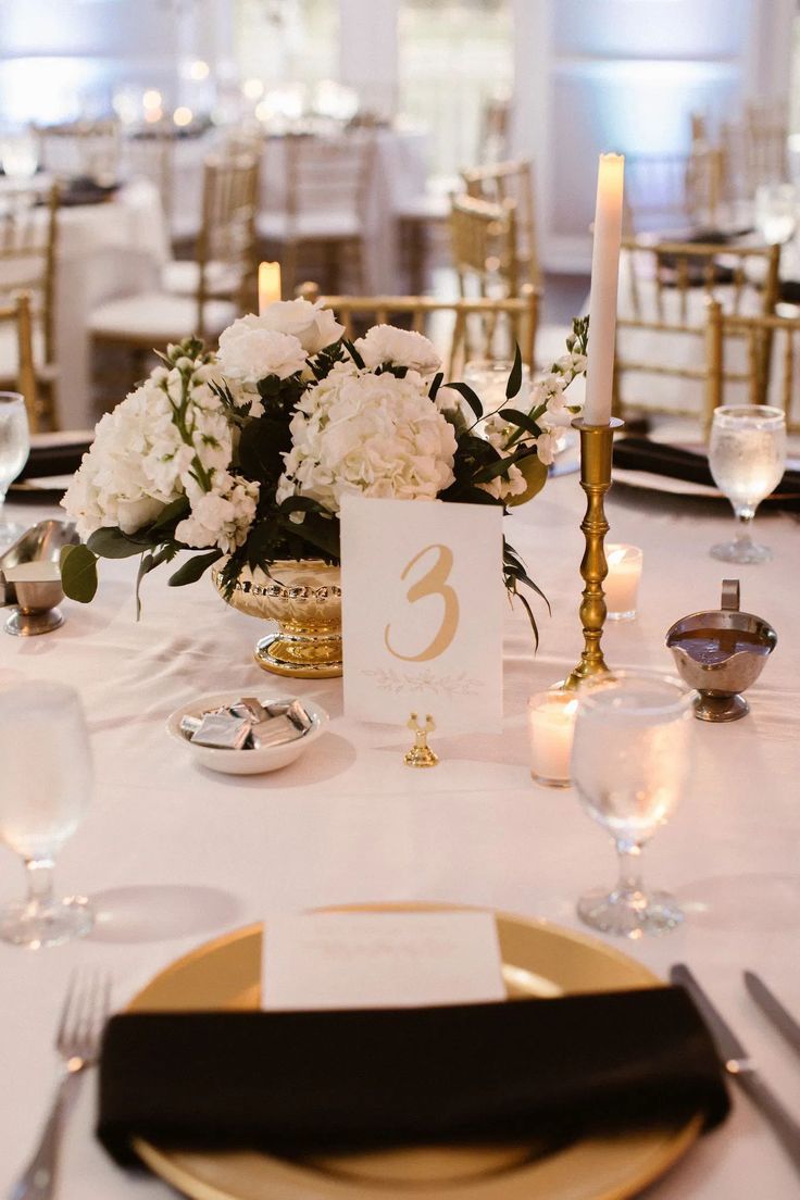 the table is set with white flowers and gold place settings for an elegant wedding reception