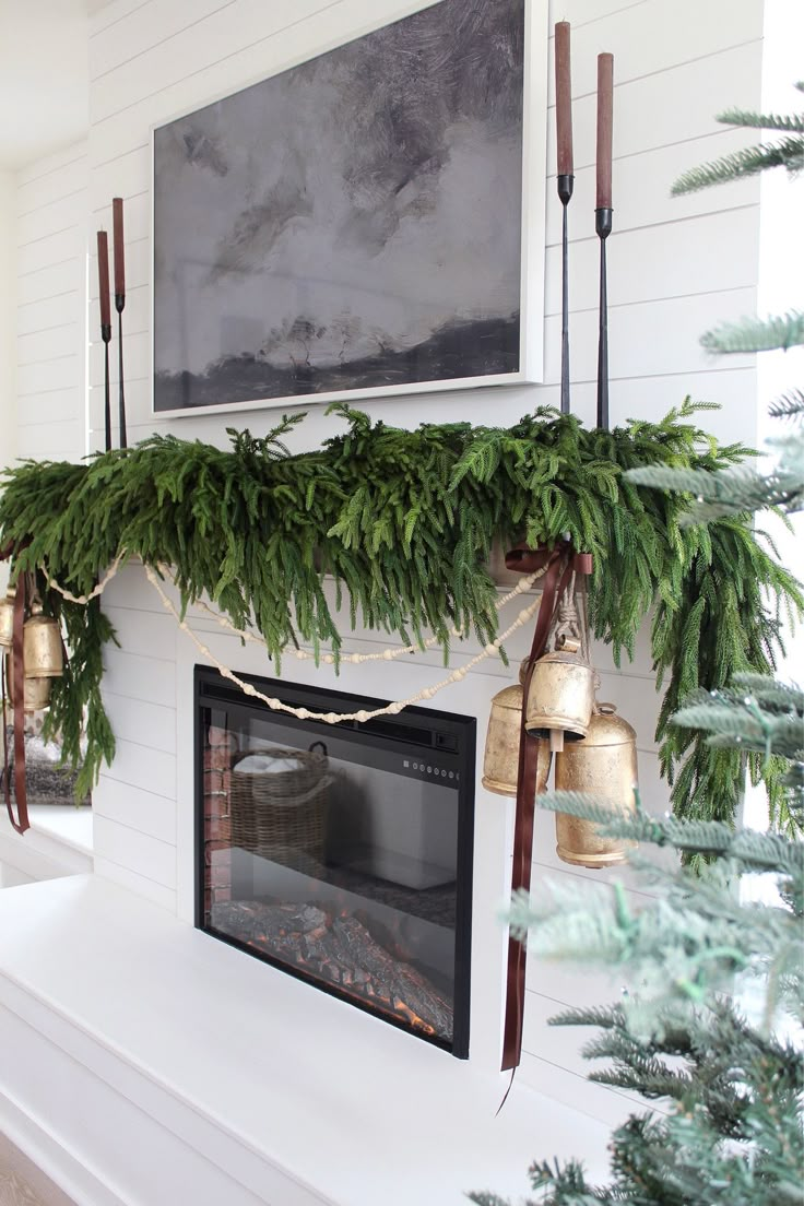 a fireplace decorated for christmas with greenery and bells hanging from the mantel above it