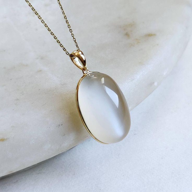 ITEM DESCRIPTION: >>The pendant is made from Solid 14K Yellow Gold. Gemstone used is absolutely natural and ethically sourced. >>Natural White Moonstones cabochon with bezel setting are studded on it with utmost precision. >>This is a minimalist design and is absolutely hassle-free and everyday jewelry. ✓ Gem: White Moonstone ✓ Gem size: 15x24 mm ✓ Gem weight: 29.04 carats ✓ Gold purity: 14K (58.33% approx.) ✓ Gold weight: 0.67 grams ✓ Gross weight: 6.48 grams The Gold purity is guaranteed and i White Moonstone Necklace For Formal Occasions, White Pendant Jewelry With Bezel Setting, Elegant White Necklaces With Large Stone, White Chalcedony Jewelry For Anniversary, Formal White Moonstone Necklace, Elegant White Necklace With Large Stone, White Gold Moonstone Round Pendant Jewelry, Elegant Moonstone Necklace With Large Stone, Luxury White Moonstone Necklaces