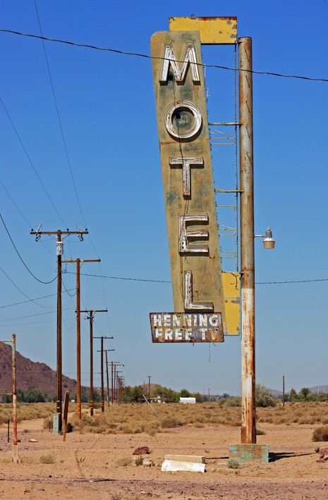 an old motel sign in the desert with power lines and telephone poles behind it,