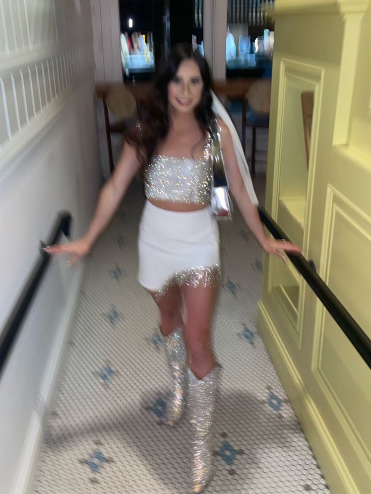 a woman in silver and white outfit walking down a hallway with her arms out to the side