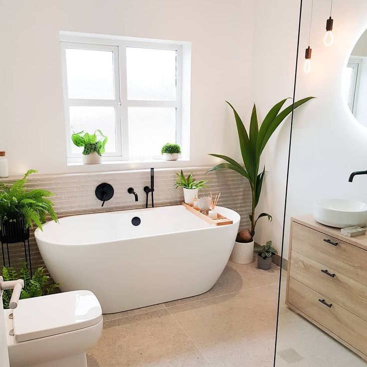 a white bath tub sitting next to a toilet in a bathroom under a large window