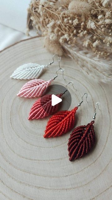 three pairs of red and silver leaf earrings on top of a piece of wood next to a pile of feathers