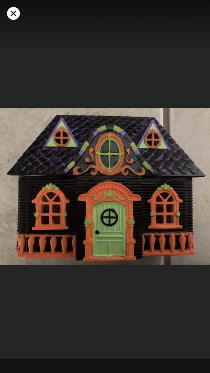 a doll house with a green door and window on the front, and an orange fence around it