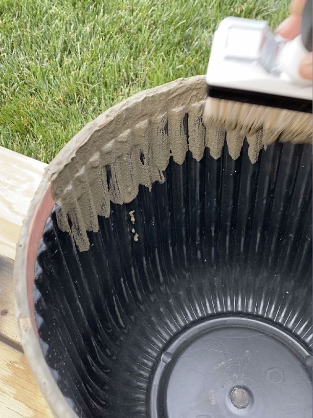 a person using a brush to clean a large bowl on the ground with grass in the background