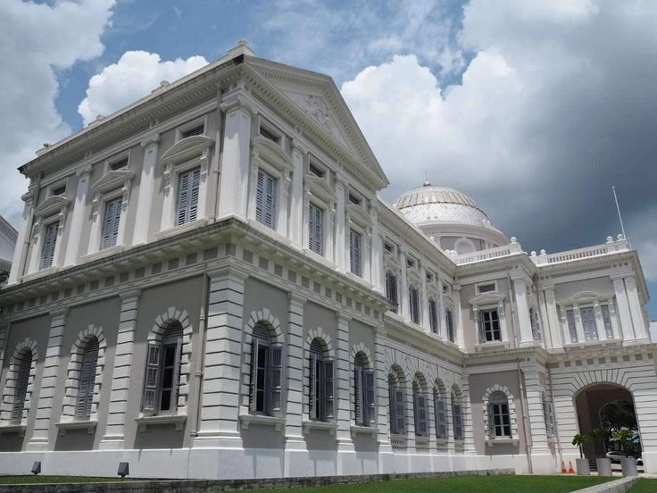 a large white building sitting on top of a lush green field under a cloudy blue sky