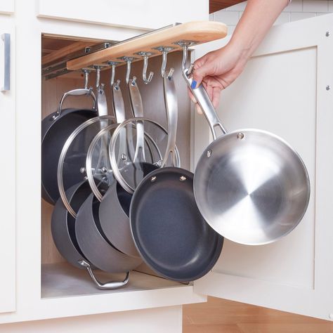 a person is holding pots and pans in a kitchen cabinet with hanging racks on the wall