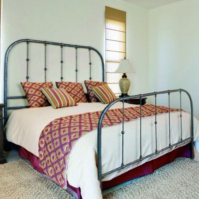 a bedroom with a metal bed frame and colorful pillows on top of the bedspread