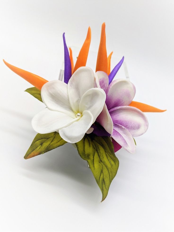 an arrangement of flowers is displayed on a white surface with green leaves and orange tips