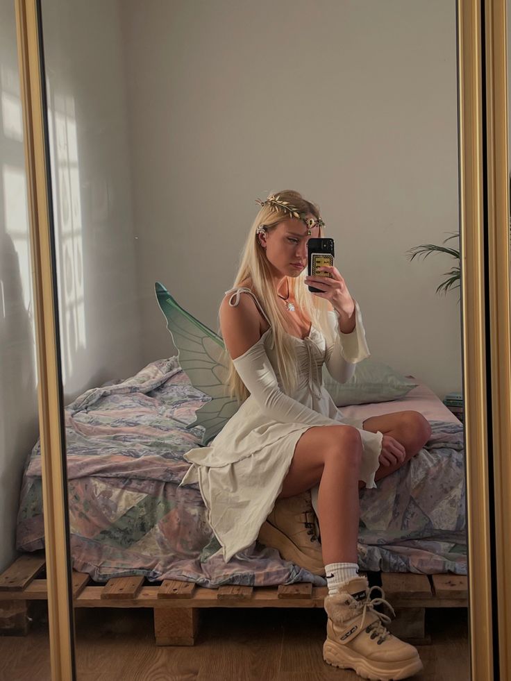 a woman sitting on a bed taking a selfie with her cell phone in the mirror