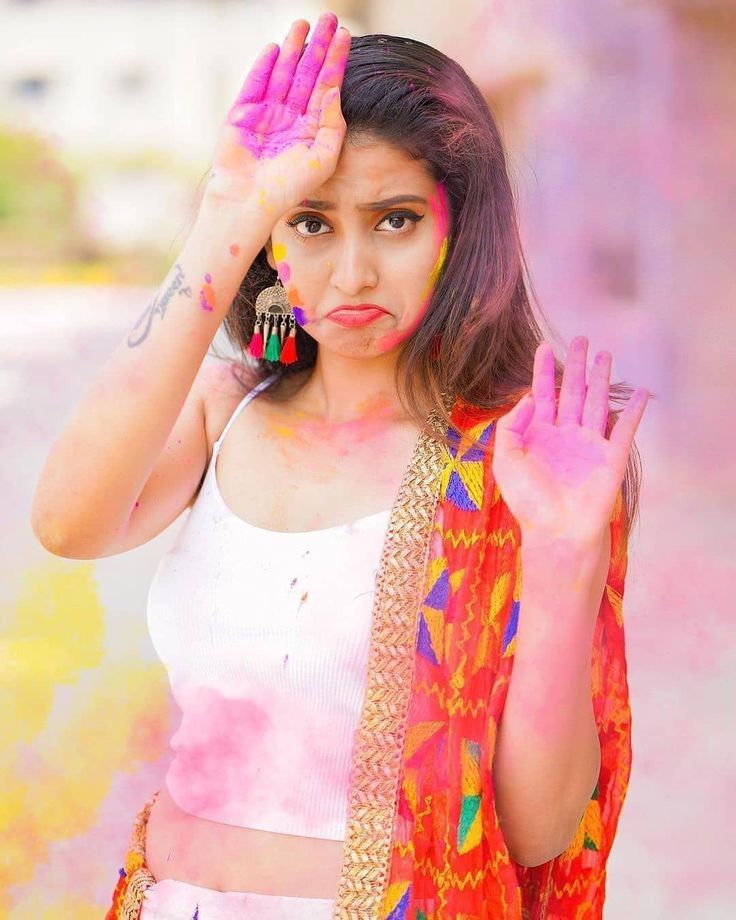 a woman with her hands in the air while she is covered in colored powder and holding her hand up to her face