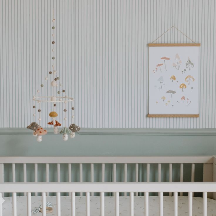 a baby crib in a nursery with a painting on the wall above it and a mobile hanging from the ceiling