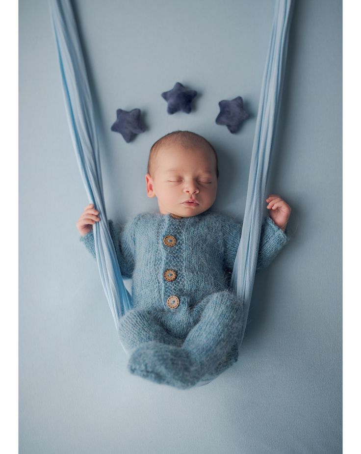 a baby is laying down in a blue outfit with stars on the wall behind him