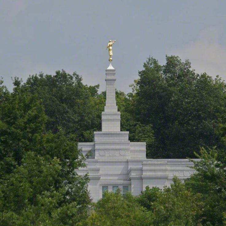 a white monument with a gold statue on top surrounded by trees