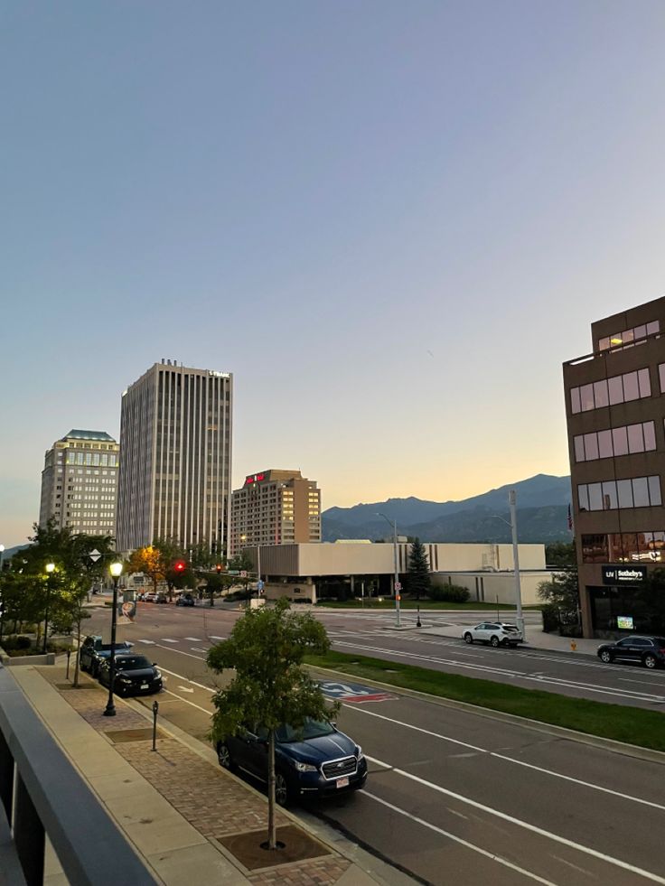 a city street with cars parked on both sides and buildings in the background at sunset